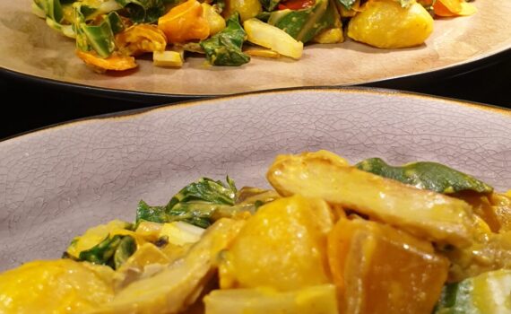 2 bunte Teller mit Mangold Gnocchi hintereinander vor einer grünen Wand; der vordere Teller ist mintfarben der hintere hellbraun; beide mit dunklem Rand; zwischen den saftigen Gnocchi leuchten die frischen knackigen Mangold Streifen hervor; halbierte Pilze sind zu erkennen und glasige Stückchen Paprika und Knoblauchscheibchen;