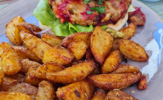 Burger mit Salat, tief rotem mit Käse überbackenem Pattie und einer großen Scheibe Champignon; davor liegen gebratene Kartoffelspalten am Teller.