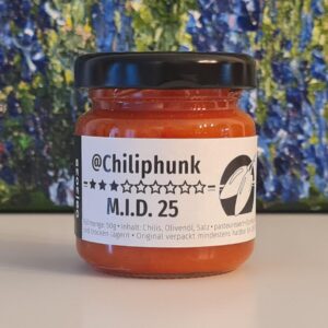 1 Glas Chilipaste Chiliphunk "M.I.D. 25" mit 3 Sternen am Etikett. Im Hintergrund steht ein Ölgemlde, von dem man nur den Fußbereich sieht. Grün-blaue Struktur mit lila Punkten.